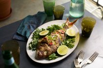Roasted whole fish dish in a table setting with glasses and napkin — Stock Photo