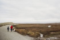 Father and son walking dog by saltmarsh and sand dunes — Stock Photo