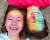 Duas crianças deitam bochecha a bochecha com tinta facial colorida rindo — Fotografia de Stock