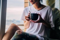 Жінка п'є каву біля вікна в сонячній кімнаті — стокове фото
