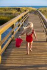 Menina de trás correndo na ponte para a praia com balde vermelho — Fotografia de Stock