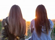Duas meninas de volta para trás assistindo o pôr do sol — Fotografia de Stock