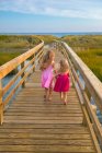 Маленькие девочки из-за бега по мосту на пляж в розовых платьях — стоковое фото
