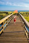 Menina de trás correndo na ponte para a praia com Red FishingNet — Fotografia de Stock