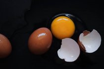 Zerbrochenes Ei mit ganzen braunen Eiern auf schwarzem Hintergrund, Draufsicht — Stockfoto