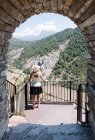 One sexy blonde woman wearing a straw hat, yellow shirt and black skirt close to an iron bar fence looking the landscape of a mountain. The scene is through an ancient stone arch. Vertical ph — Stock Photo