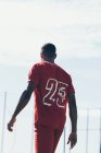 Vue arrière du footballeur afro-américain marchant sur un terrain gazonné — Photo de stock