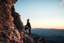 Climber woman with helmet and harness. Silhouette at sunset on the mountain. Profile. Resting looking at the climbing route. Doing via ferrata in the mountains. — Stock Photo