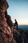 Bergsteigerin mit Helm und Gurt. Silhouette bei Sonnenuntergang auf dem Berg. Profil. Ruhe beim Blick auf die Kletterroute. Klettersteige in den Bergen. — Stockfoto