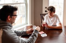 Adolescente menino e seu pai jogando cartas na mesa juntos. — Fotografia de Stock