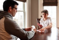 Підлітковий хлопчик і його батько грають карти за столом разом . — стокове фото