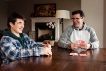 Отец и сын-подросток смеются, играя в карты за столом. — стоковое фото