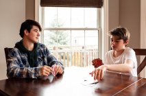 Два подростка вместе играют в карты за кухонным столом. — стоковое фото