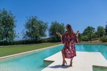 Chica rubia posando en verano con un vestido junto a la piscina - foto de stock