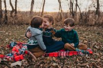 Drei Geschwister sitzen lachend auf rotkarierter Decke — Stockfoto
