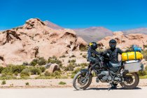 Donna in piedi accanto a moto turismo su strada polverosa in Bolivia — Foto stock