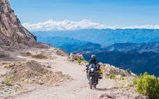 Человек едет на мотоцикле по гравийной дороге в Боливии — стоковое фото