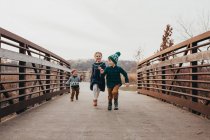 Frères et sœurs qui courent ensemble sur le pont vers la caméra — Photo de stock