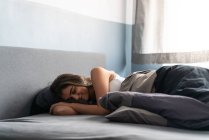Средний снимок молодой женщины, спокойно спящей в своей комнате на кровати в утреннем свете. — стоковое фото