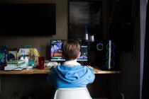 Rückansicht von Teen Boy, der am Spielcomputer am chaotischen Schreibtisch spielt — Stockfoto