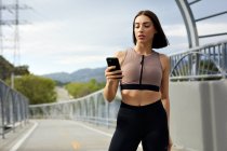 Messaggi di testo jogger sullo smartphone mentre sei in piedi sul ponte — Foto stock