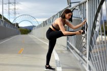 Longueur totale de la femme étirant la jambe tout en faisant de l'exercice sur le pont — Photo de stock