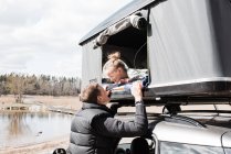 Padre mirando a su hija en una carpa en la azotea mientras acampaba - foto de stock