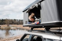 Girl looking out of roof top tent at a view of a lake whilst camping — Stock Photo