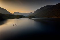 Early morning paddle boarders sail across Crummock Water a lake in the Lake District part of the UNESCO World Heritgae Centre in Cumbria. — Stock Photo