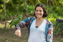 Mujer posa con una sonrisa mientras lleva su brazo a un guacamayo en un campamento - foto de stock