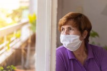 Elderly watches through the window of her house, while being confined by the coronavirus quarantine..... — Stock Photo