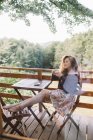 Молодая красная женщина пьет кофе на балконе домика на дереве — стоковое фото