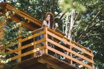 Молодая женщина стоит на балконе домика на дереве — стоковое фото
