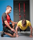 Personal trainer ajudando cliente com treinamento de suspensão no ginásio — Fotografia de Stock