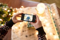 Man taking pictures on smartphone carefully wrapped Christmas present — Stock Photo