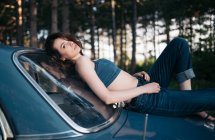 Femme hipster couchée sur une voiture vintage dans la forêt. — Photo de stock