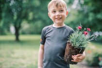 Feche-se de um menino sorridente segurando uma planta — Fotografia de Stock