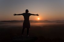 Silhouette of girl at the top of a mountain at sunrise with arms out — Stock Photo