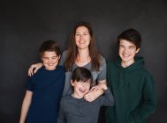 Mutter mit drei älteren Jungen lacht vor schwarzem Hintergrund. — Stockfoto