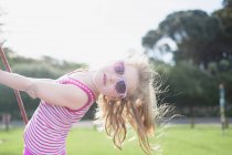 Chica joven jugando en swing usando gafas de sol - foto de stock