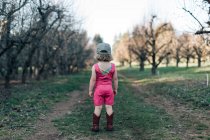 Ein junges Mädchen steht in einem Obstgarten und trägt ein Trikot und Cowgirl-Stiefel. — Stockfoto