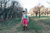A young girl stands in an orchard wearing a leotard and cowgirl boots. — Stock Photo