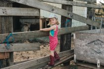 A young girl stands on a fence wearing a leotard and cowgirl boots. — Stock Photo