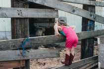 A young girl stands on a fence wearing a leotard and cowgirl boots. — Stock Photo
