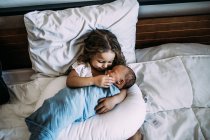 Young girl holding newborn baby brother on bed — Stock Photo