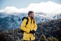 Jovem com casaco amarelo e mochila nas montanhas. — Fotografia de Stock