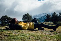 Jovem com casaco amarelo e mochila deitada na montanha. — Fotografia de Stock