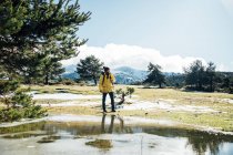 Молодий чоловік з жовтим піджаком і рюкзаком біля ставка в горі . — стокове фото