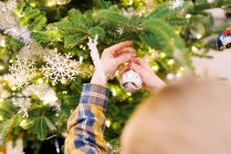 Niño pequeño poniendo adornos en su árbol de Navidad - foto de stock