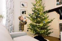 Маленький мальчик надевает украшения на свою елку — стоковое фото